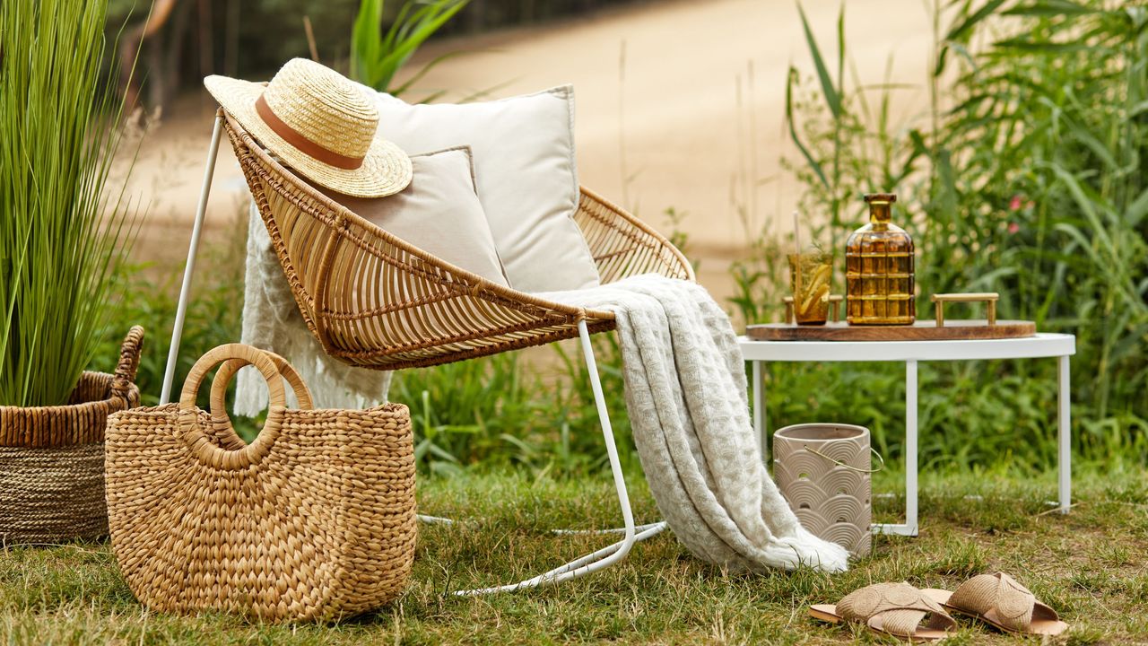 A wicker chair, strewn with white blankets and cushions, sits on a verdant green hilltop in the English countryside