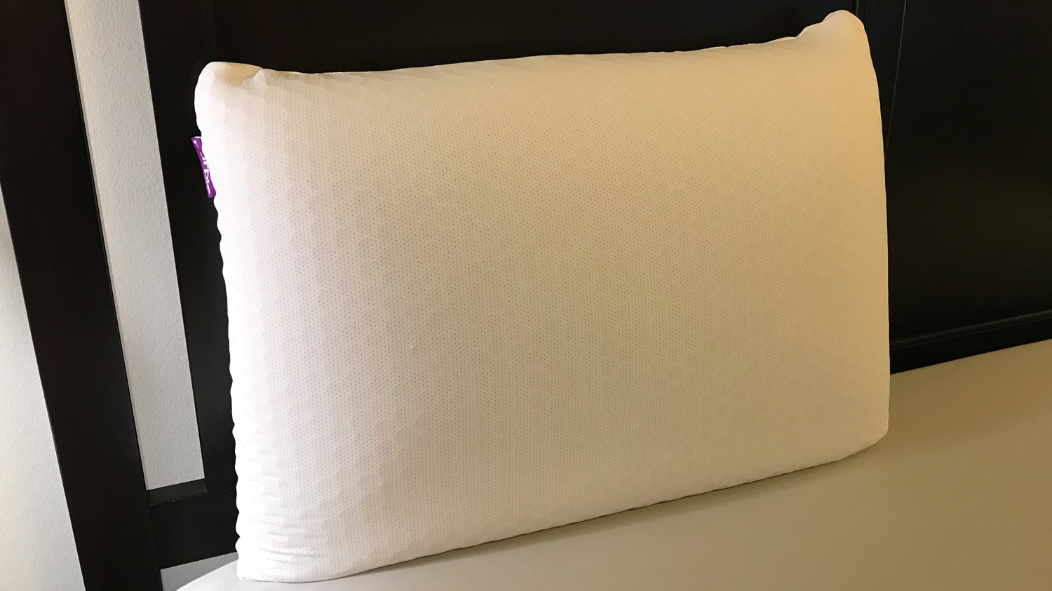 O Purple Harmony Pillow em uma cama, encostado na cabeceira da cama