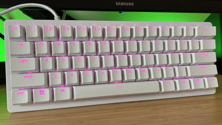 White Razer Huntsman V3 Pro Mini gaming keyboard on a wooden desk with green back lighting