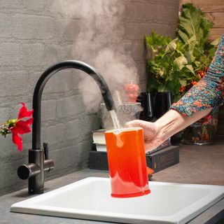 Black Qettle boiling water tap filling an orange jug over a white kitchen sink