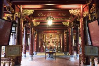 Red lacquered walls and golden statues inside the Bach Ma Temple in Hanoi