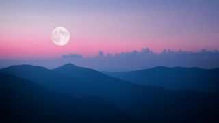 full moon rising over mountains