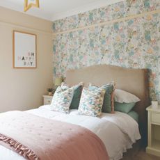 A pastel bedroom with a feature wall covered in a floral wallpaper and a neighbouring wall painted in a soft peach colour