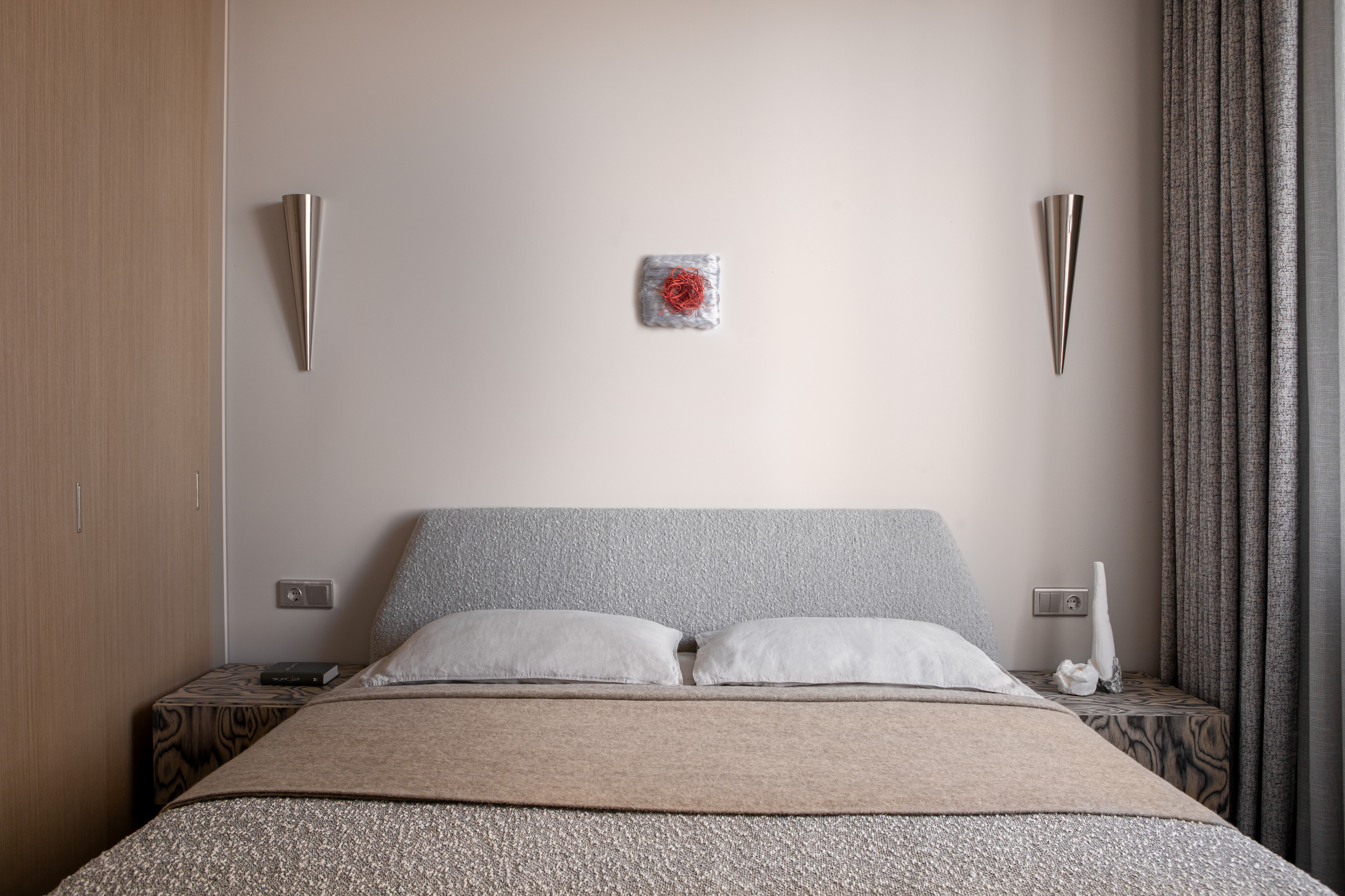 A bedroom with grey bedding, white walls and simple brushed metal wall lights