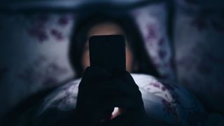 Young woman scrolls through her phone at night