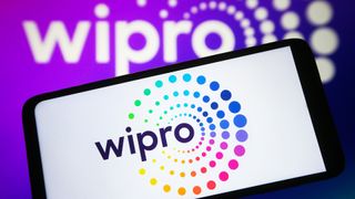 Wipro logo pictured on a smartphone screen with branding displayed on computer screen in background.