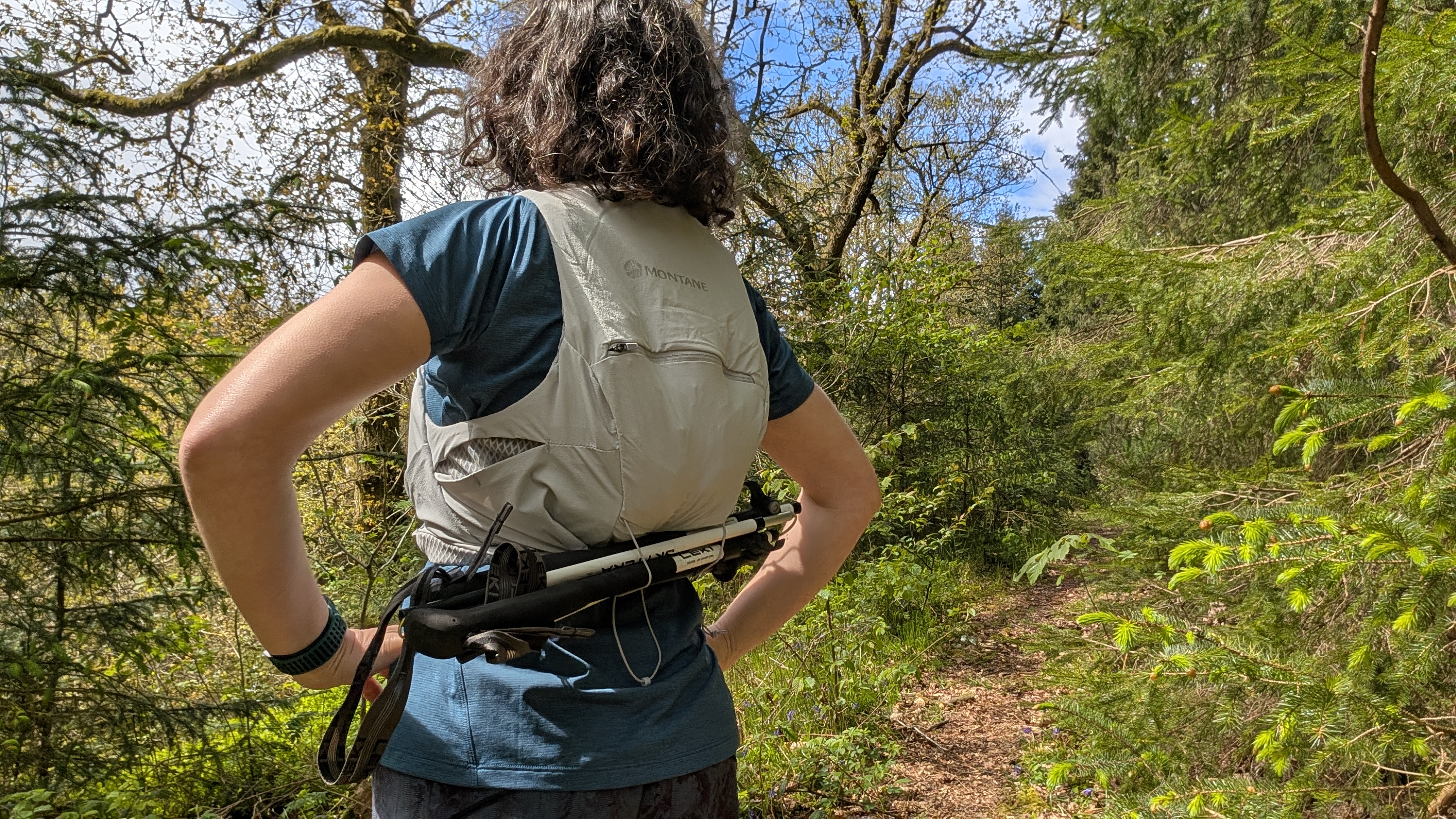 A woman trail runner stand with her hands on her hips showing the running poles attached to the bottom of her Montane Gecko hydration vest