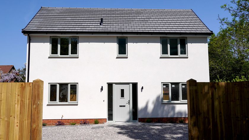 New two-storey house with white render and grey windows and doors and gravel drive with wooden fence in foreground