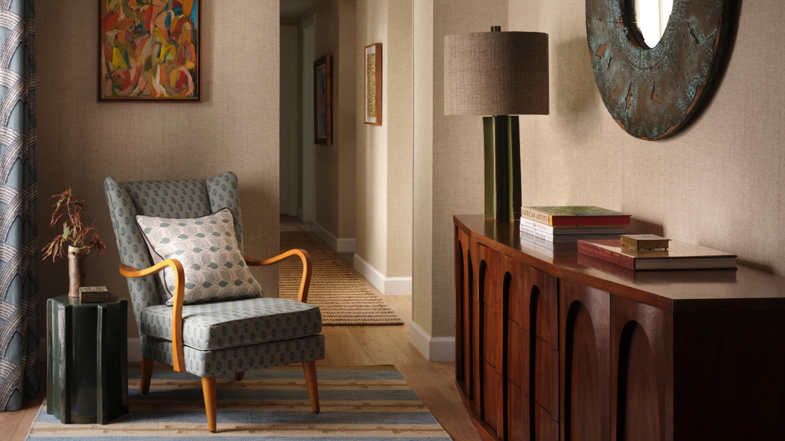 Entryway with a blue vintage armchair, striped rug, dark wood cabinet, sculptural mirror and colorful contemporary artwork.
