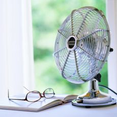 Metal desk fan beside open book with glasses on top