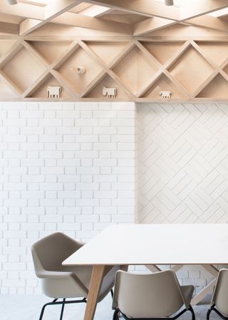 a dining table with chairs. In this extension there is a brick wall painted white with different brick layout patterns and above it a contrasting wooden wall/ ceiling