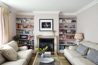 beige living room with blush pink bookcases, matching couches, fireplace, coffee table, drapes, artwork
