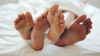 Two pairs of feet in a bed with a white sheet.