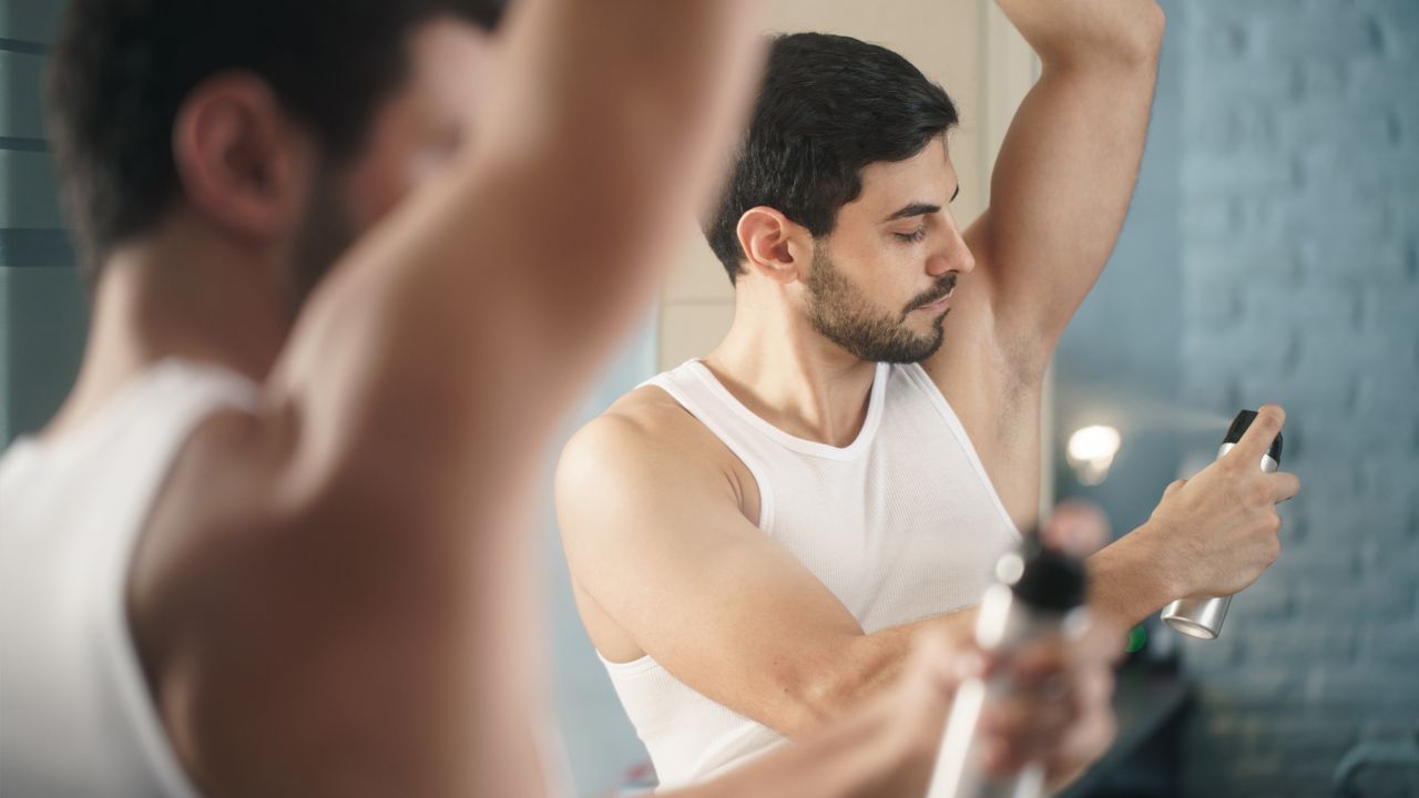 Man spraying deodorant under onto his armpit