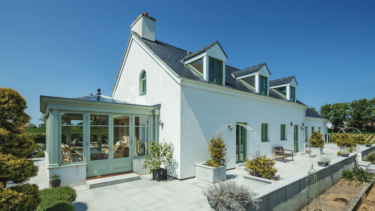 white house with dormer windows in roof and green wooden orangery to side