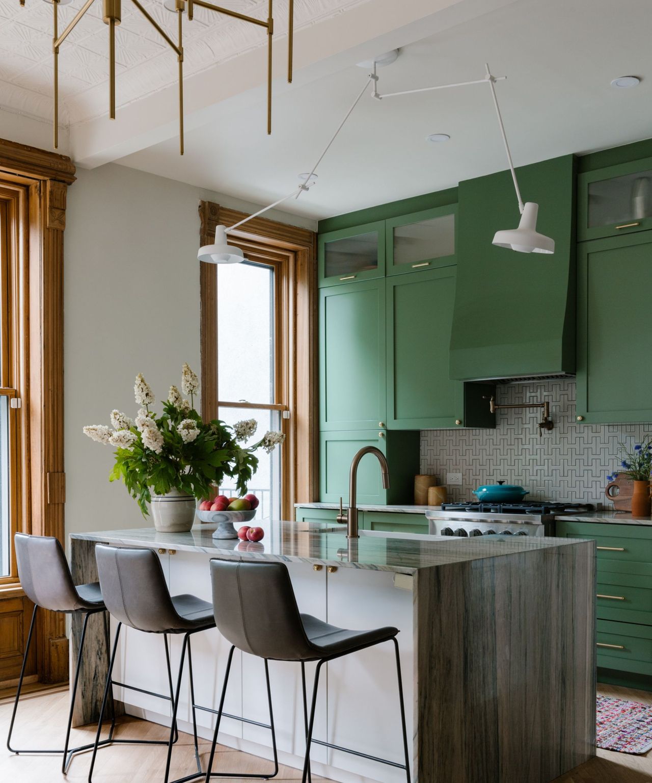 A green brownstone kitchen with a wooden island and three barstools