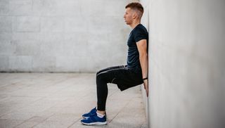 Man performing wall sit, leaning with his back against the wall, with his knees bent at 90° and feet flat on the floor.