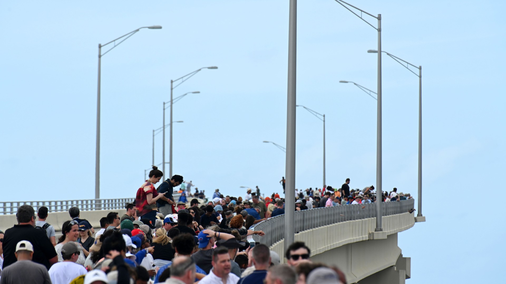 حشد من الناس يوجهون الكاميرات نحو السماء نحو سلسلة من النار والدخان بعيدًا في الخلفية