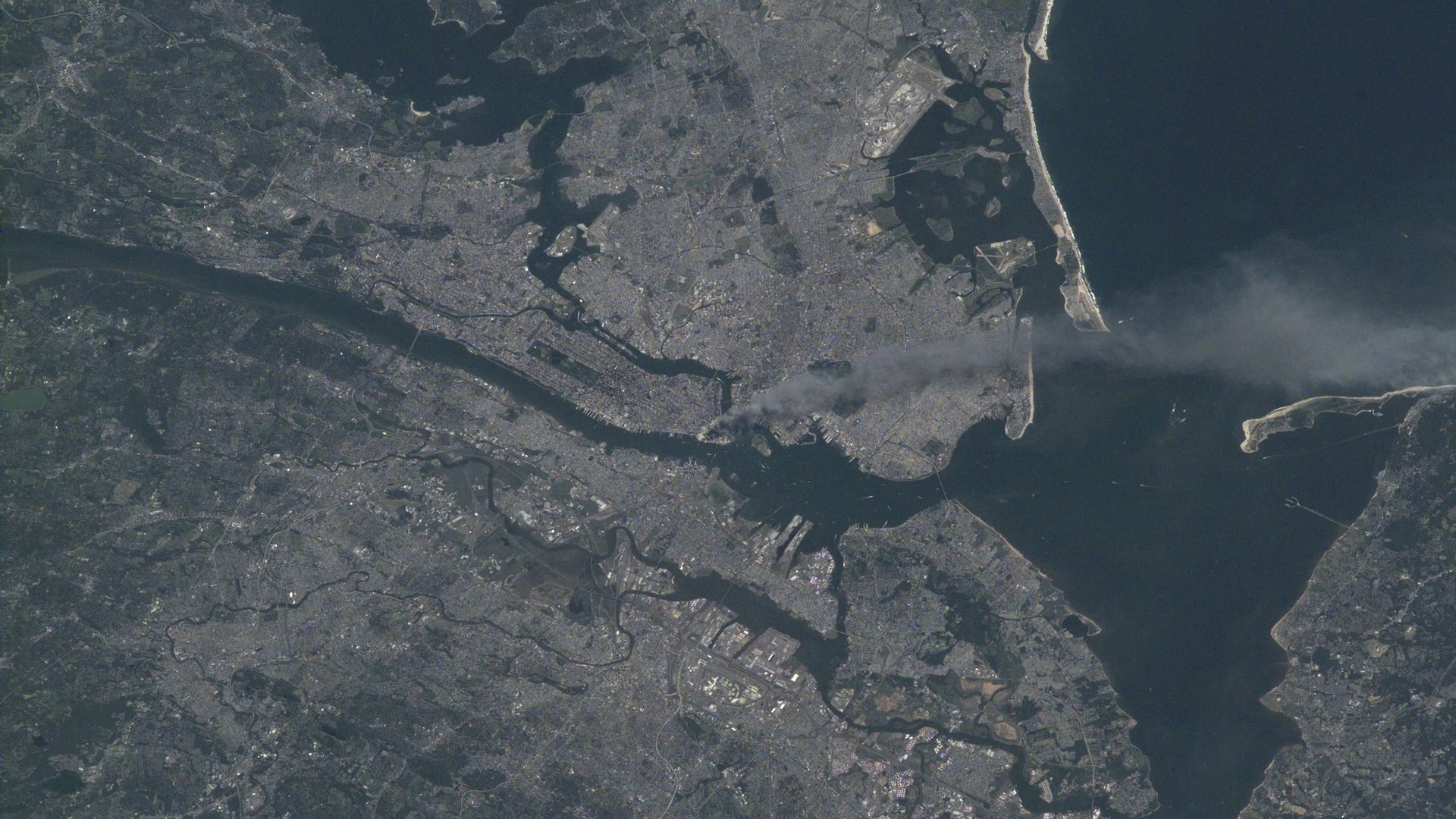 satellite photo of a large city on a bay, with a river running through it and smoke rising from the center of the city