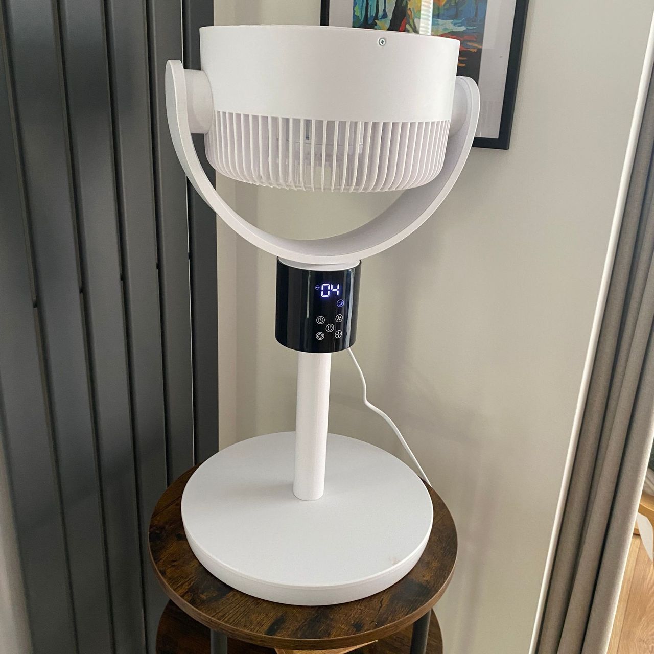 The Silentnight Airmax Pro360 Pedestal Fan in oscillating mode on a wooden side table next to a vertical radiator