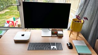Mac mini, Studio display, keyboard, mouse set up on a wooden desk 