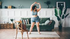 Woman exercising in front of couch with an open laptop on a chair