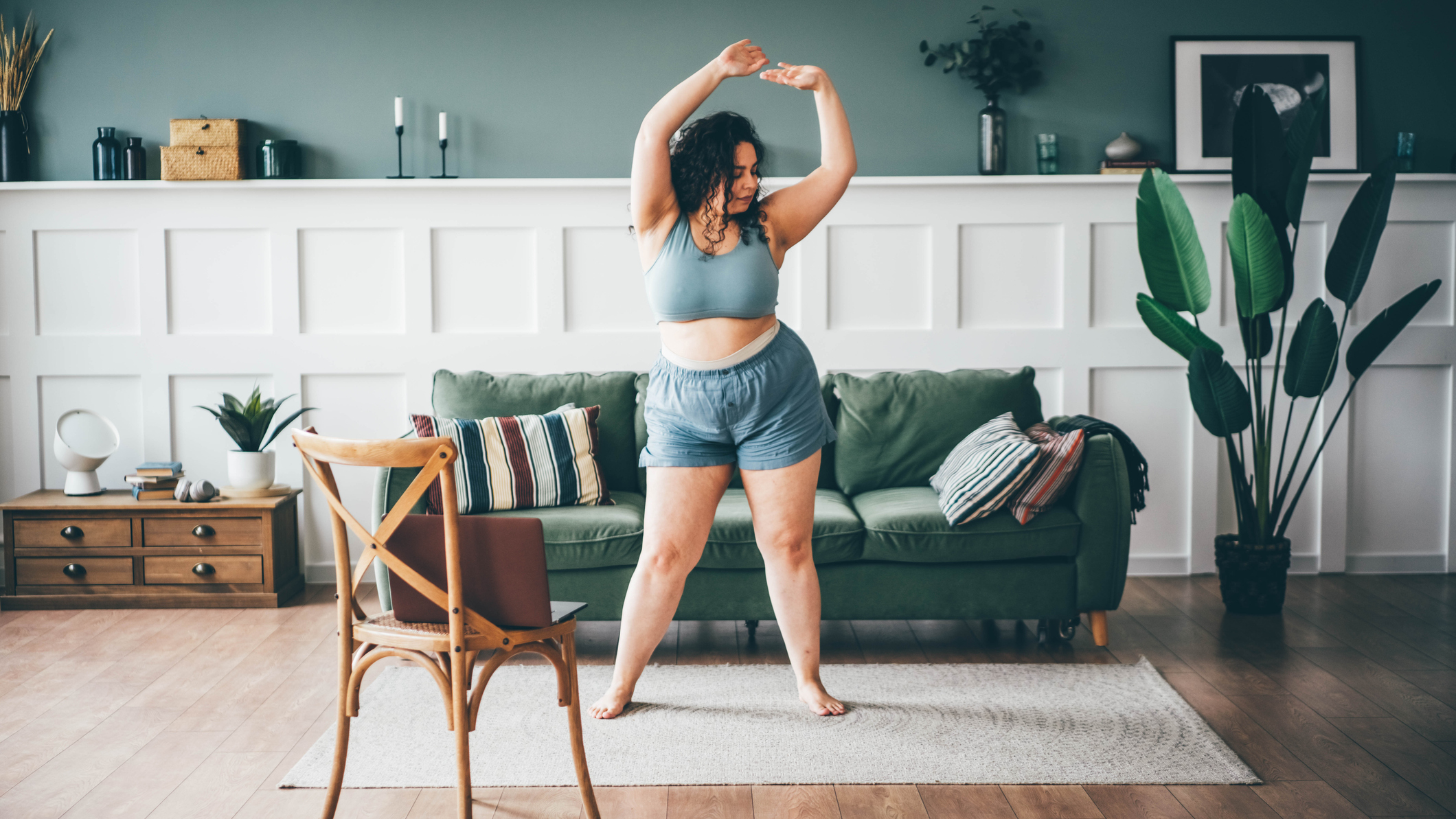 Woman exercising in front of couch with an open laptop on a chair