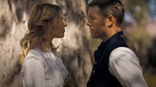 Sienna Miller and Sam Worthington stand facing each other in front of a tree in Horizon: An American Saga - Chapter 1.