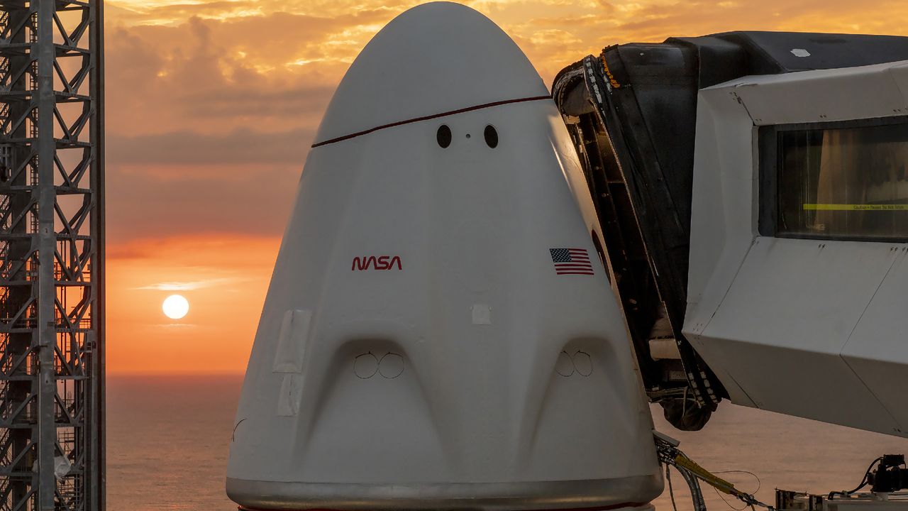 A white space capsule with NASA and US logos on the pad with the sun low on horizon