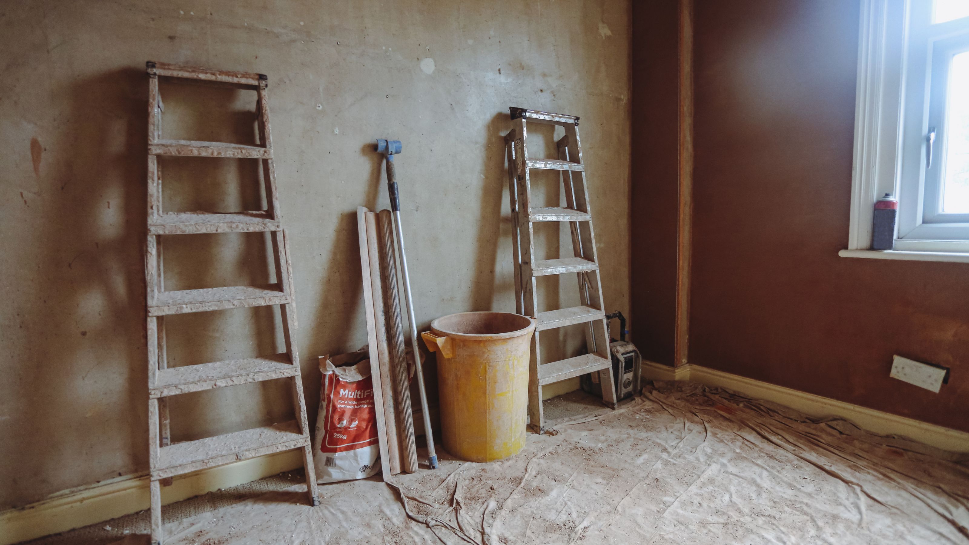 Ladders against the wall and bucket and plaster mix in a room being renovated