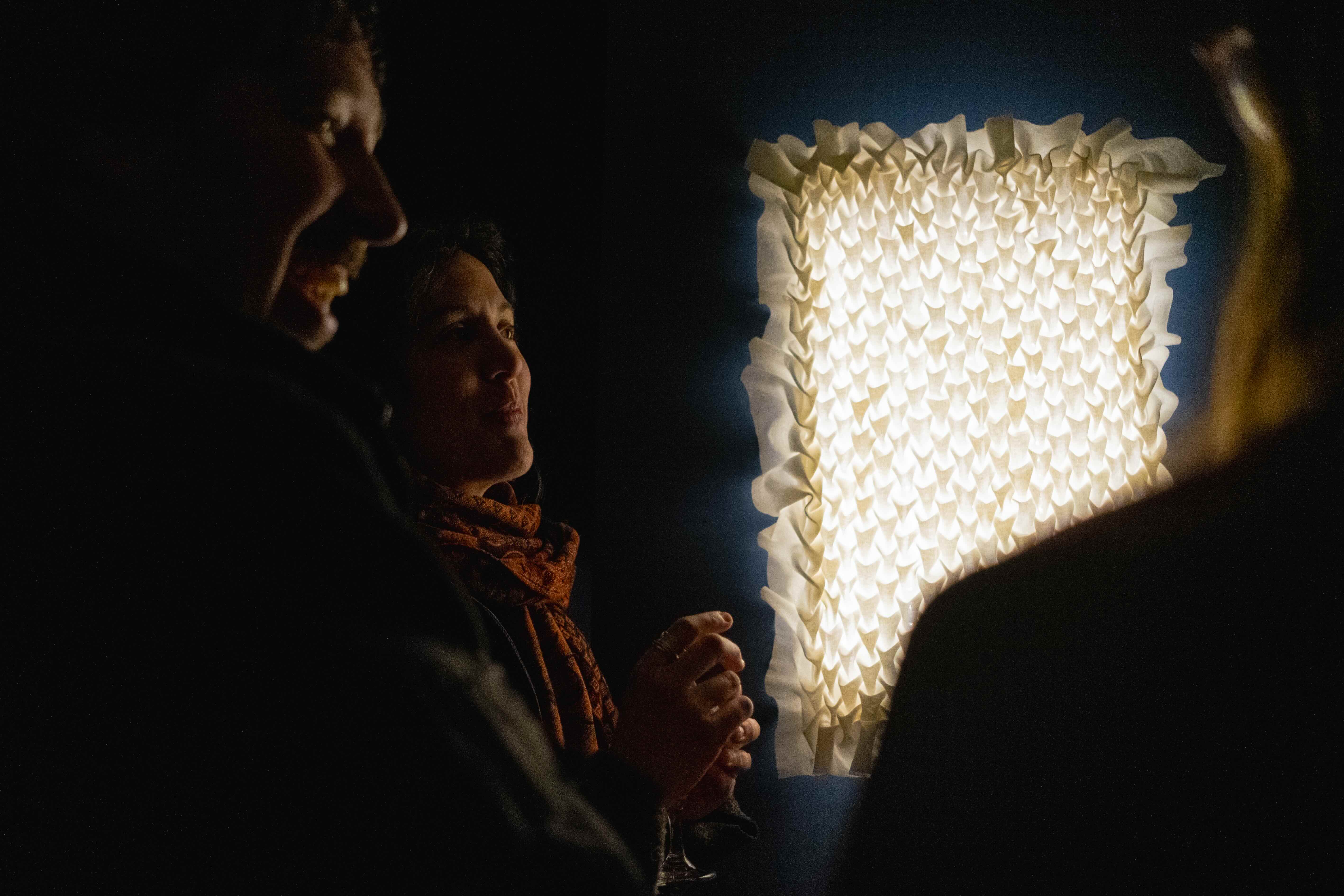 people gather around a glowing textile wall lamp