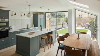 large kitchen diner with picture window, skylights, dark sage green kitchen, pendant lights above island and wall light above hob area