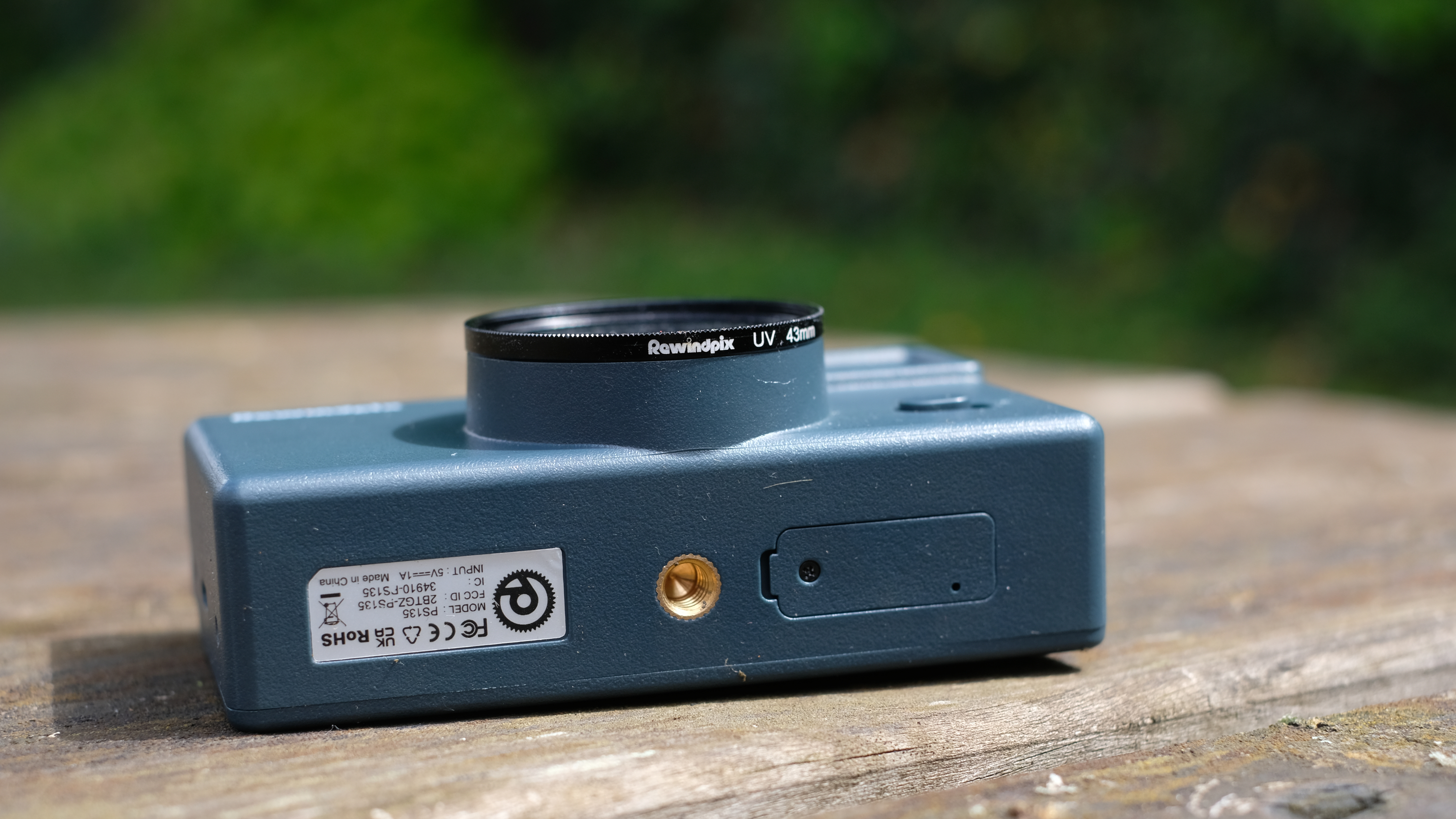 Photograph of RewindPix digital compact camera showing bottom with tripod mount and filter attached to lens