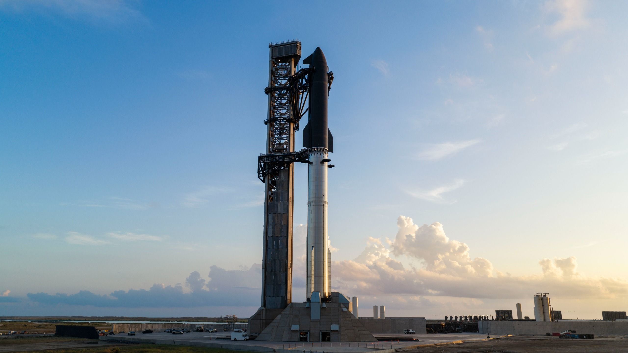 A towering SpaceX Starship rocket stands at Starbase's Pad 2 against a rich, cloudy blue sky.
