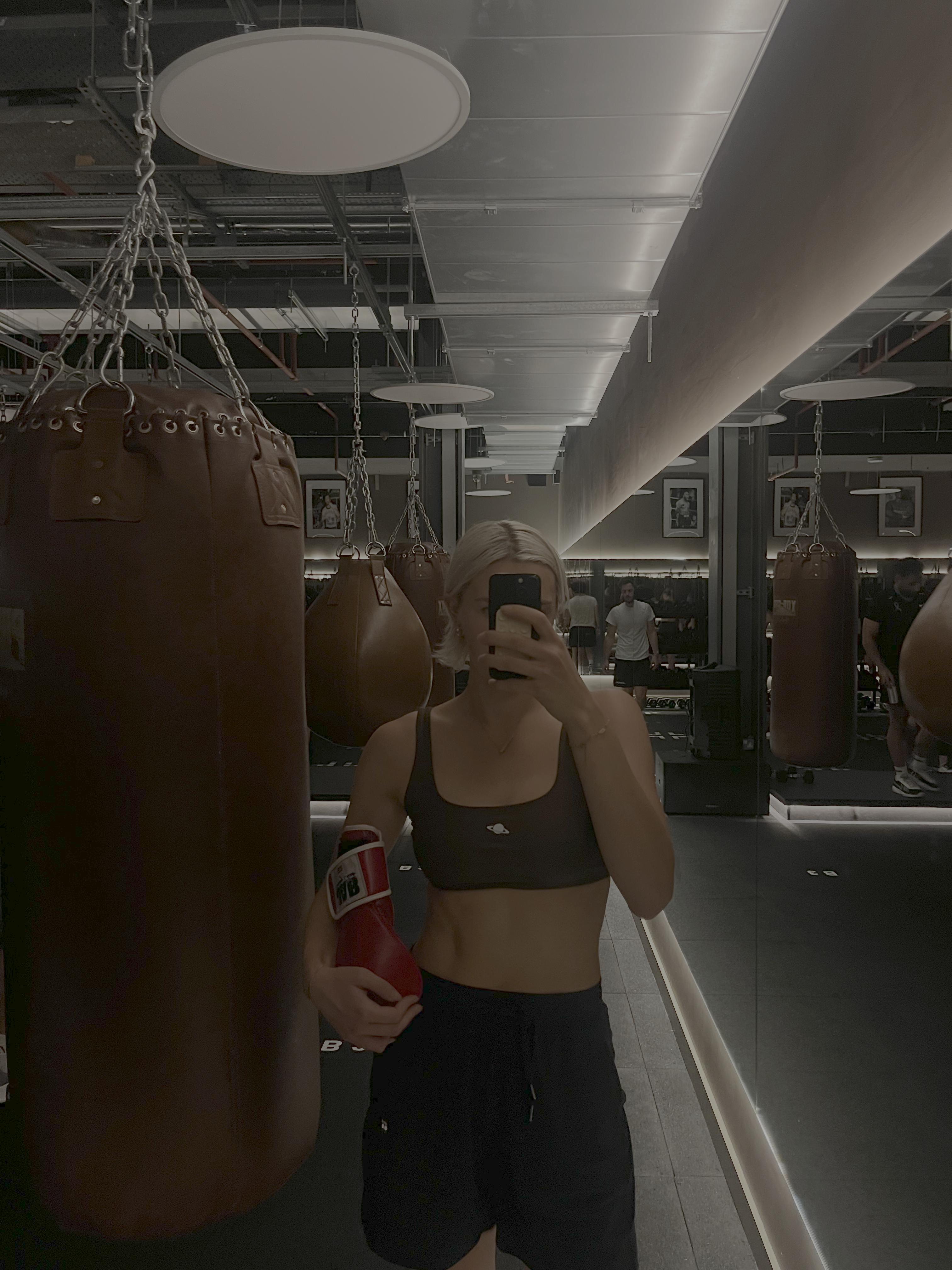A woman taking a mirror selfie whilst holding boxing gloves in a boxing gym