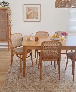 A beige dining area with wooden chairs, a dining table, and a rug