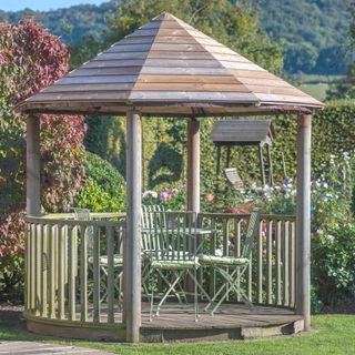 wooden gazebo in garden with vintage table and chairs