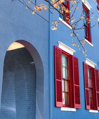 A blue painted house exterior with an arch and red shutters