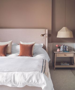 A light pink bedframe an white bedding, deep red cushions and a light wood bedside table.