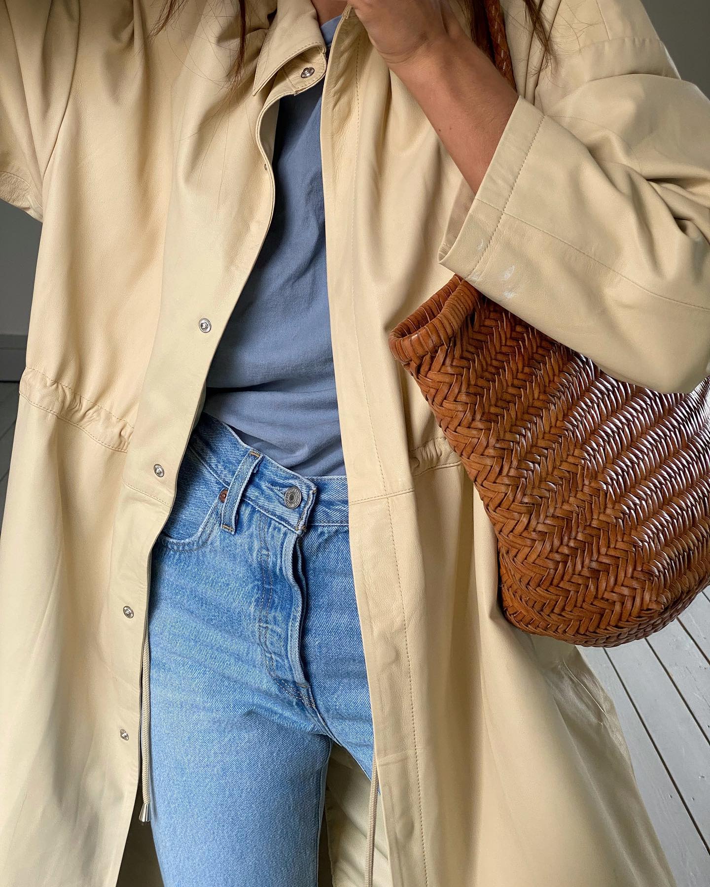 close-up mirror selfie of Marianne Smyth wearing a butter-yellow jacket, gray tee, high-waisted jeans, and a Dragon Diffusion woven leather bag