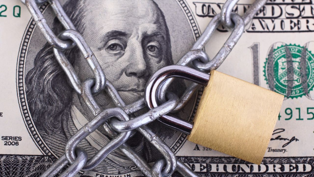 Padlock and chain wrapped around a hundred dollar bill