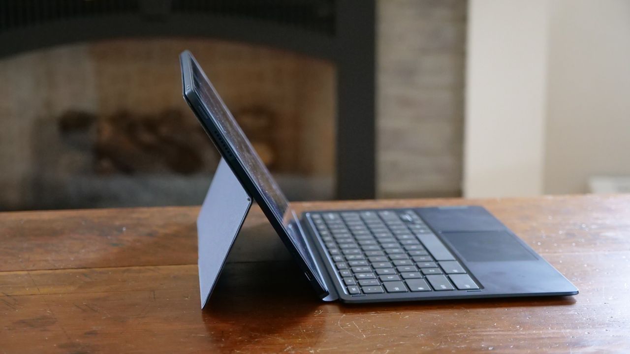 A side-view of a laptop on top of a wooden desk. A kickstand attached to the back of the display holds the screen upright at an angle