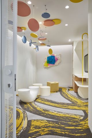 A colourful office room with hanging installation of pink blue and yellow dots on the ceiling and brightly coloured carpet with yellow paths