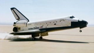 a black and white winged spacecraft touches down on its main gear on a dry lakebed