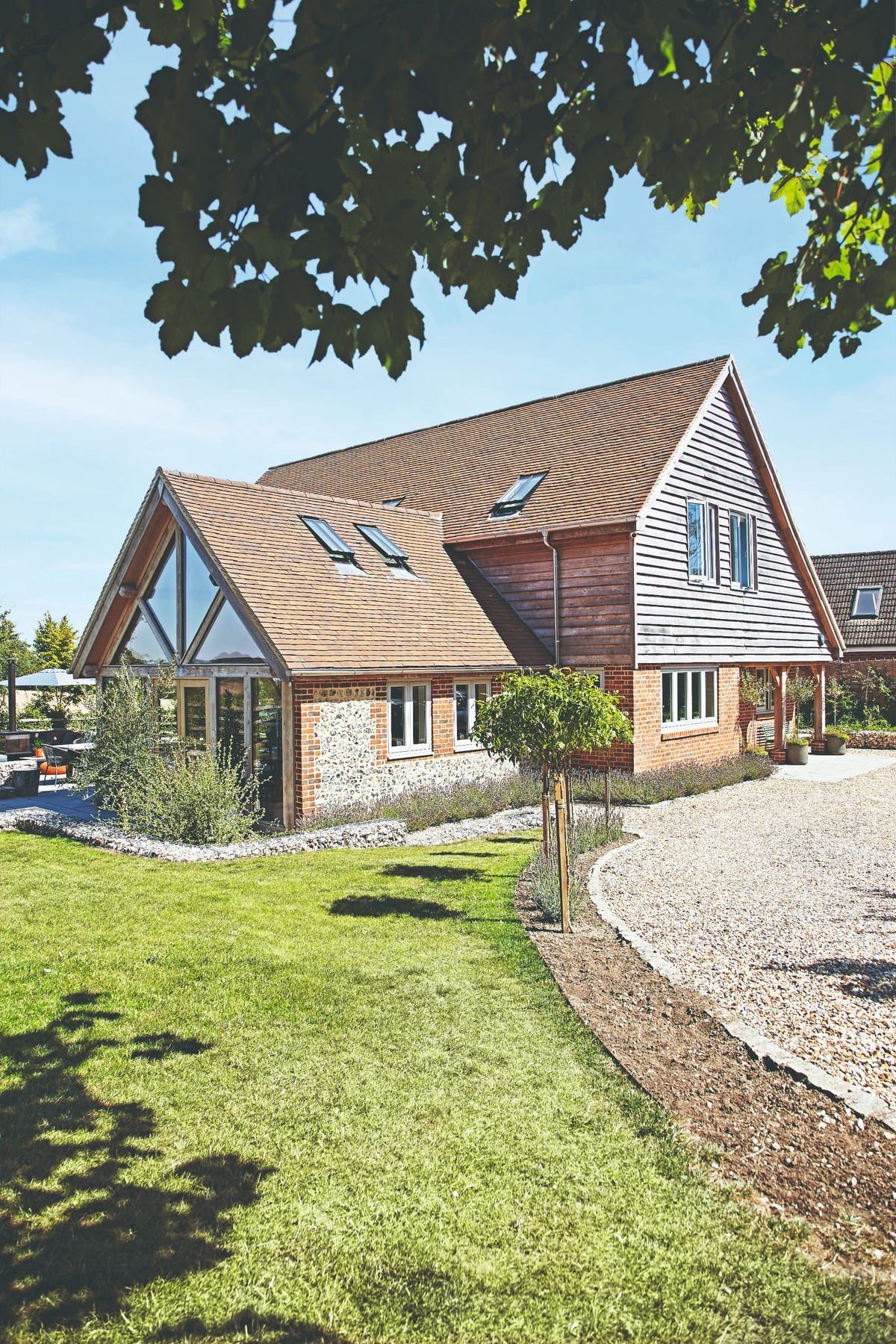 A part red-brick, part timber clad house approached by a gravel driveway and green lawn