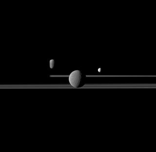 Three of Saturn's moons appear in a somber group portrait along with the northern, sunlit ringplane. Rhea (949 miles or 1,528 kilometers across) is closest to Cassini spacecraft, which took the photograph, and appears largest at the center of the image.