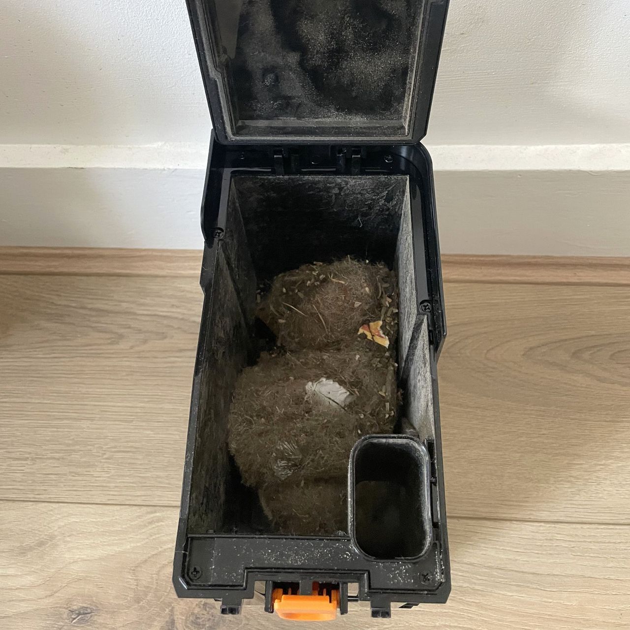 Dust canister of the Shark PowerDetect UV Reveal robot vacuum, full of dust and hair, sitting on wood-effect flooring