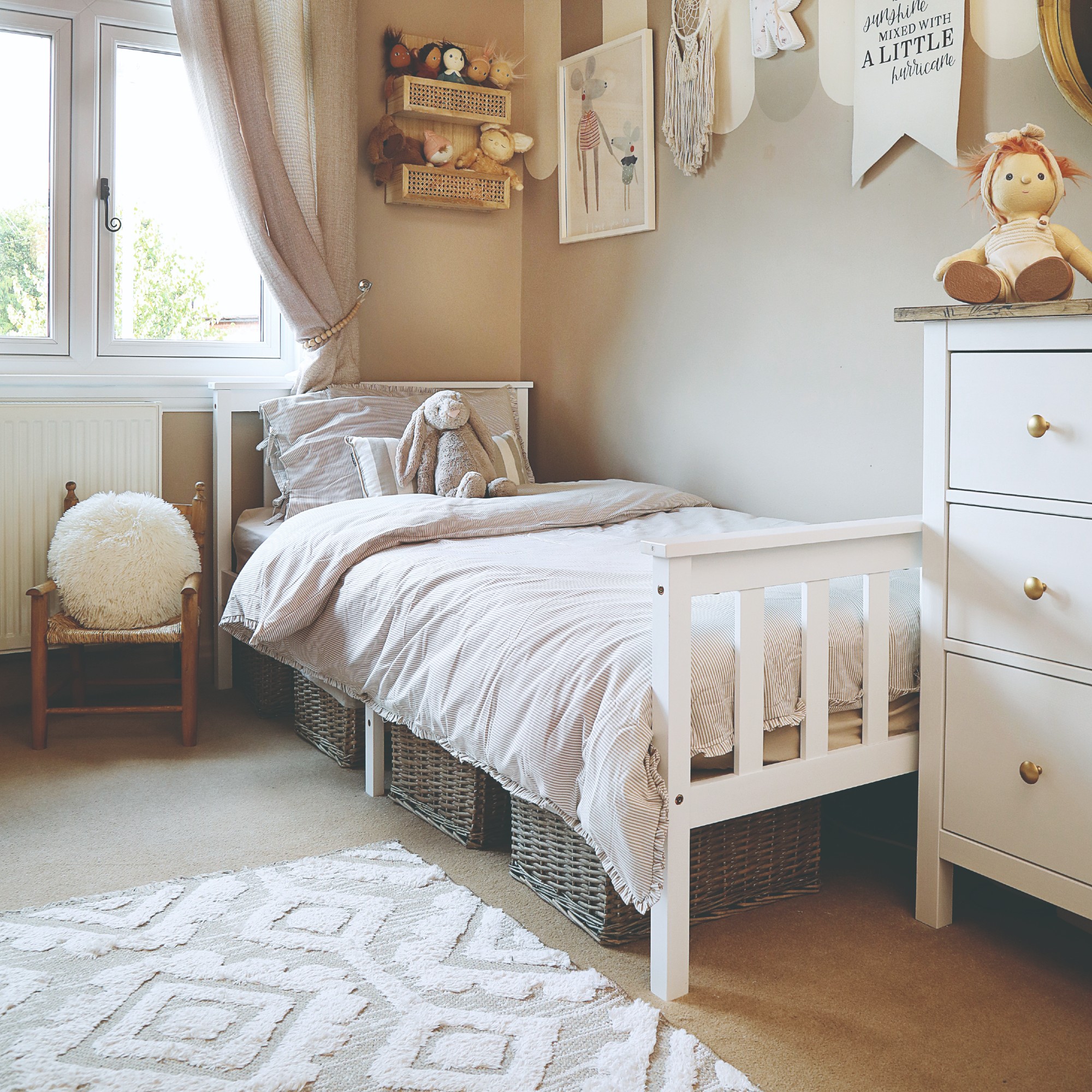 A neutral child's room with a white bed and chest of drawers and light carpeted floor with a patterned rug on top