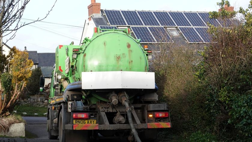 A bright green septic tank emptying lorry in front of a house with solar panels on the roof