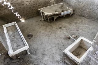 A small room with the remains of a bed, a chest, and a shelf